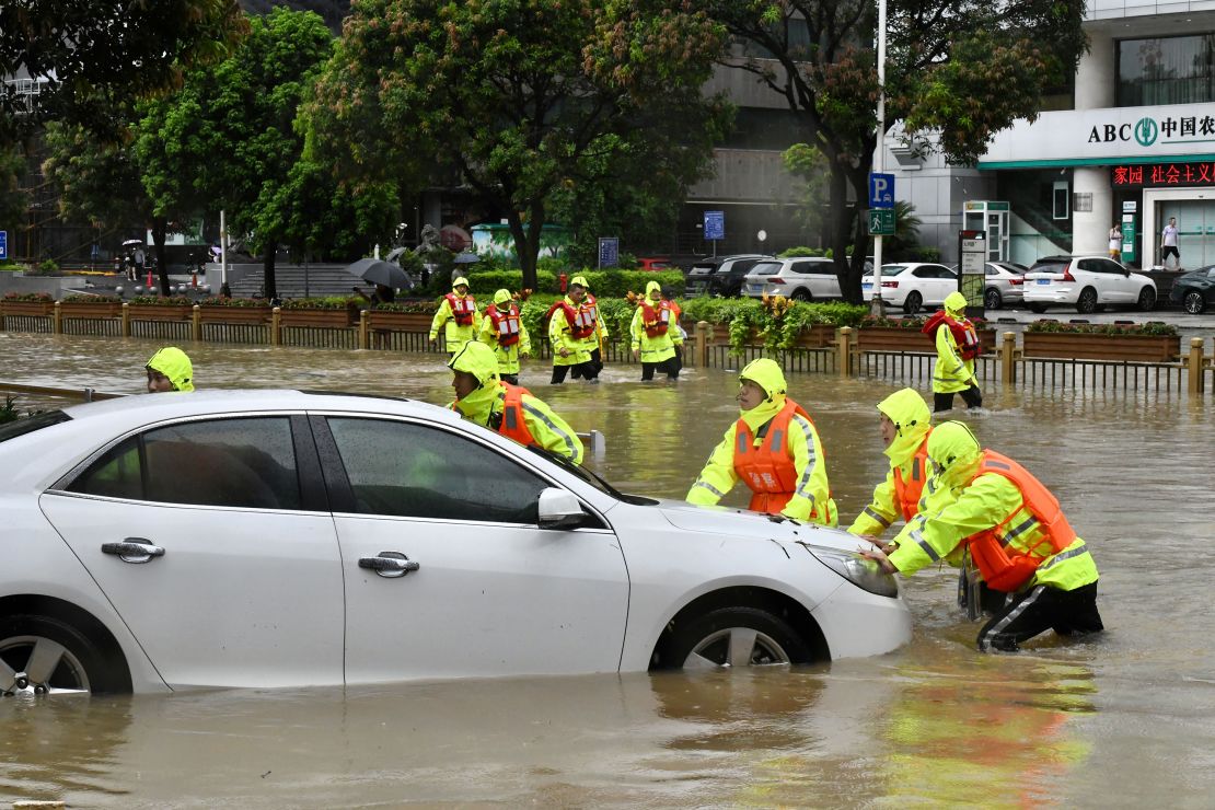 Rescuers push a trapped car in a flooded street.