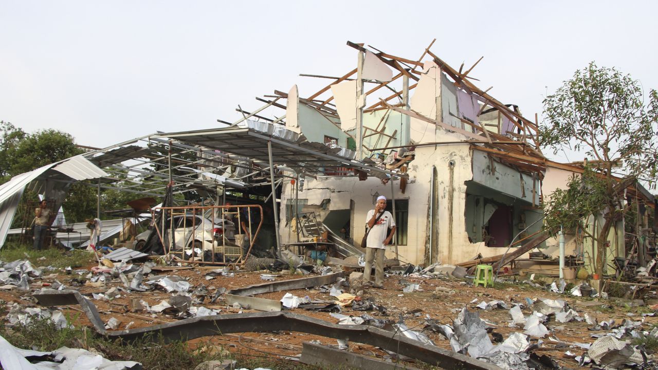 People speak on their phones in front of a house damaged by the explosion.