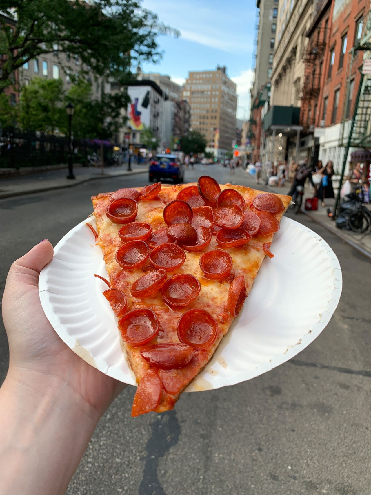 A slice of pepperoni pizza held on a New York City street.