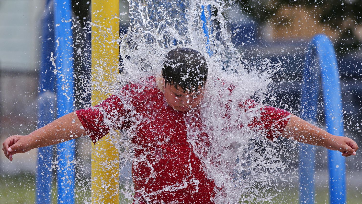 Graiden Therrien, 11, takes shelter from the sweltering heat by waiting for the automated water bucket to overturn onto his head at Harrington Park in New Bedford, Mass. on Monday, July 31, 2023. (Peter Pereira/The Standard-Times via AP)