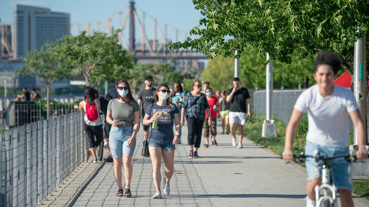 People wearing masks walk in Gantry Plaza State Park, Long Island City on May 30, 2020 in New York City.