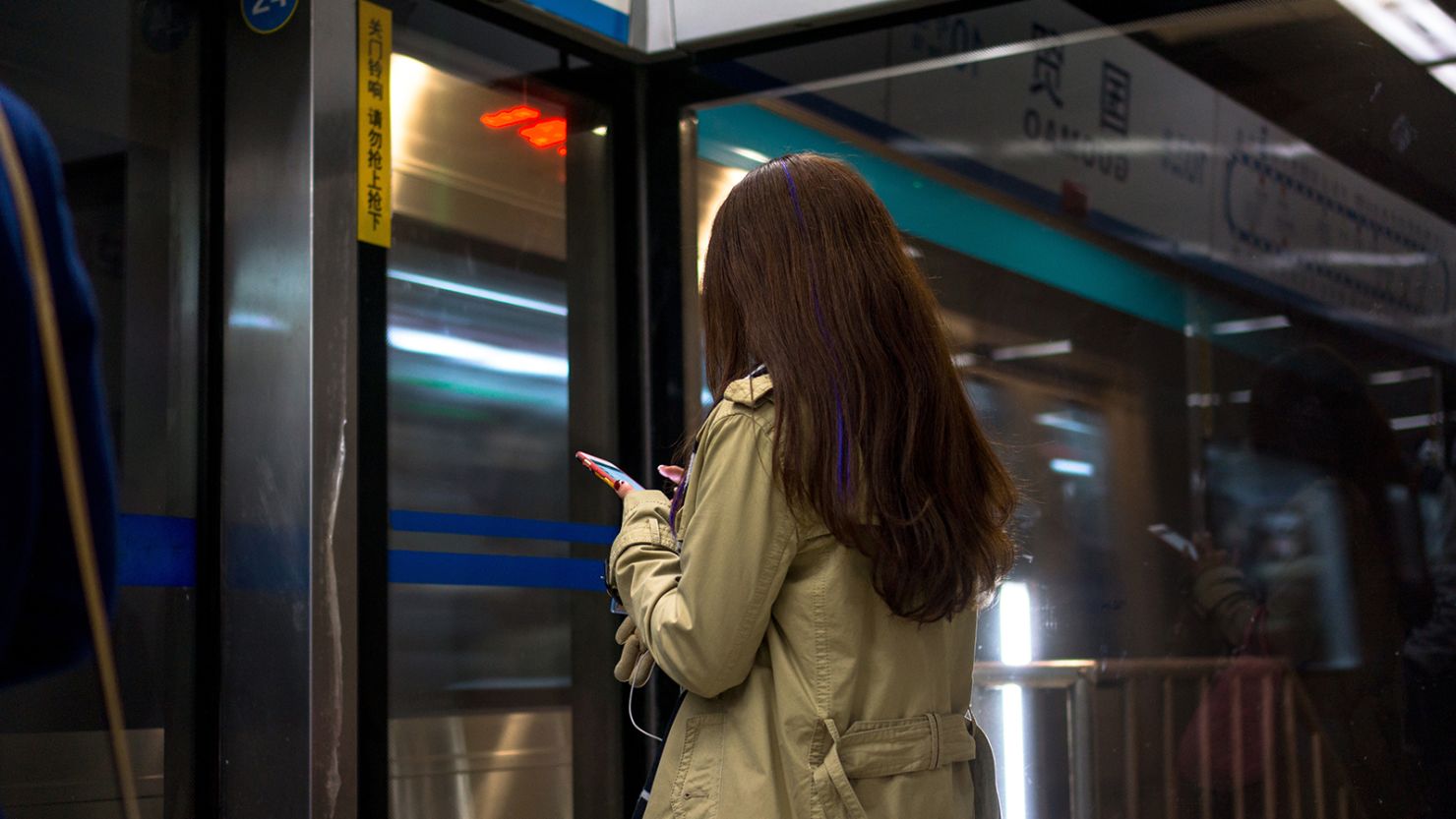 Passengers read their smart phones while waiting for the subway train in Beijing.