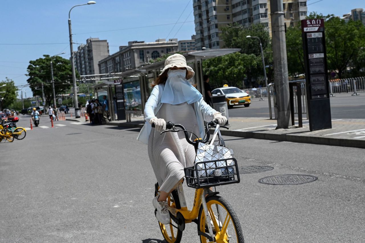 TOPSHOT - A woman wearing sun protective clothing rides a bike along a street during hot weather conditions in Beijing on July 6, 2023. (Photo by Jade Gao / AFP) (Photo by JADE GAO/AFP via Getty Images)