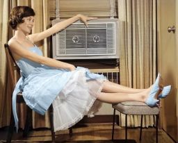 1960s Smiling Woman Sitting Propping Legs Up On Stool Resting Hand On Top Of Looking At Air Conditioner. (Photo by Debrocke/Classicstock/Getty Images)