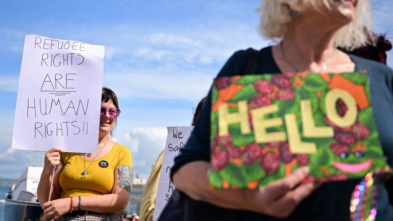 People hold up placards to welcome migrants ahead of their expected arrival at the Bibby Stockholm accommodation barge in southwest England on August 7, 2023. 