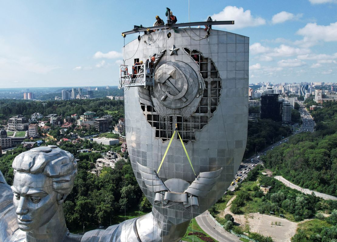 Workers remove the Soviet-era emblem from the motherland monument in Kyiv on August 1, 2023. 