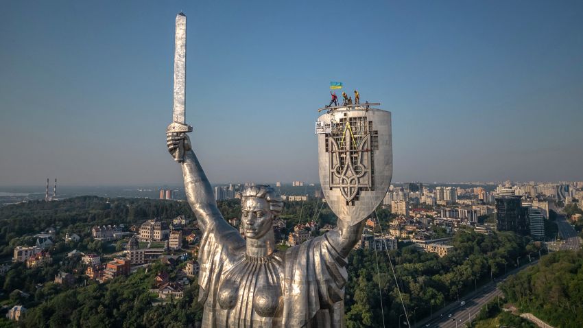 Steeplejacks wave the Ukrainian flag after finishing installing the coat of arms of Ukraine on the shield of the 62 metre Motherland Monument in Kyiv, on August 6, 2023, amid the Russian invasion of Ukraine. The Ukrainian trident replaced the coat of arms of the former Soviet Union, which was removed earlier this month. (Photo by Roman PILIPEY / AFP) (Photo by ROMAN PILIPEY/AFP via Getty Images)