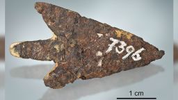 Fig. 1. a--b. a) Overview of the Mörigen arrowhead. Note adhering bright sediment material. Remnants of an older label on the left of the sample number. Total length is 39.3 mm. Photograph: Thomas Schüpbach. b) side view of the Mörigen arrowhead. Layered texture is well visible. Point is to the right.