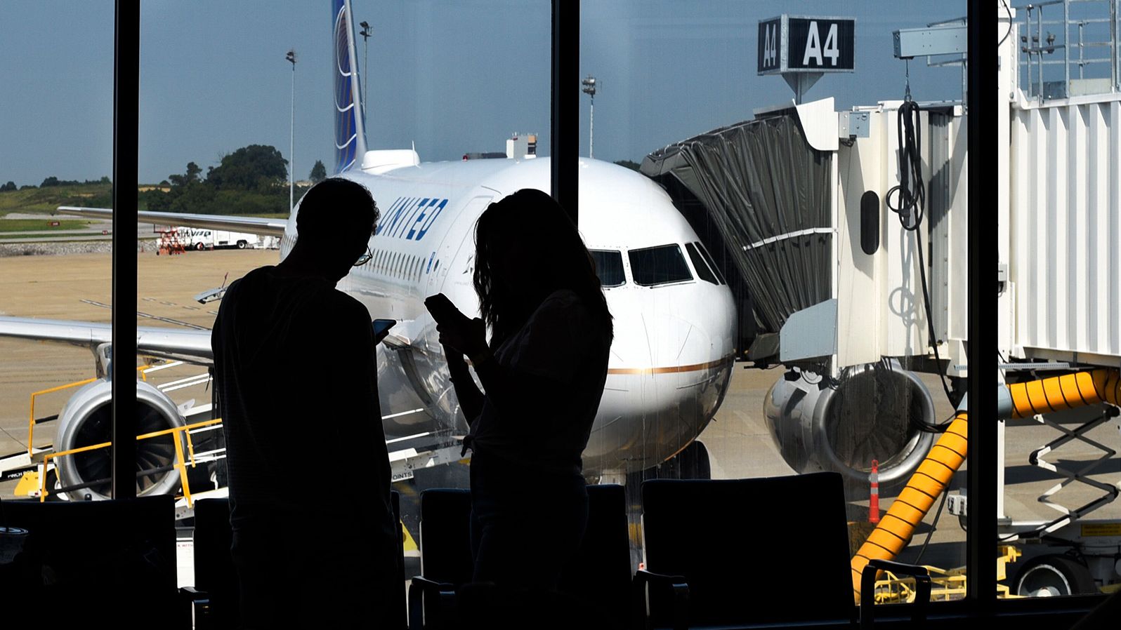 NASHVILLE, TENNESSEE - SEPTEMBER 4, 2019: A couple silhouetted in front of a window use their smartphones in the terminal gate area before boarding a plane at Nashville International Airport in Nashville, Tennessee.