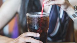 woman hand drinking glass of cola with ice, unhealthy lifestyle concept