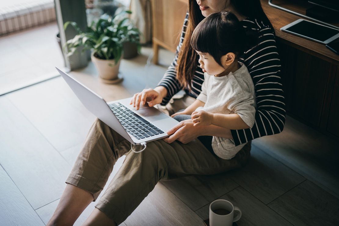 Cropped shot of a young Asian mother using laptop and working from home while taking care of little daughter in self isolation during the Covid-19 health crisis