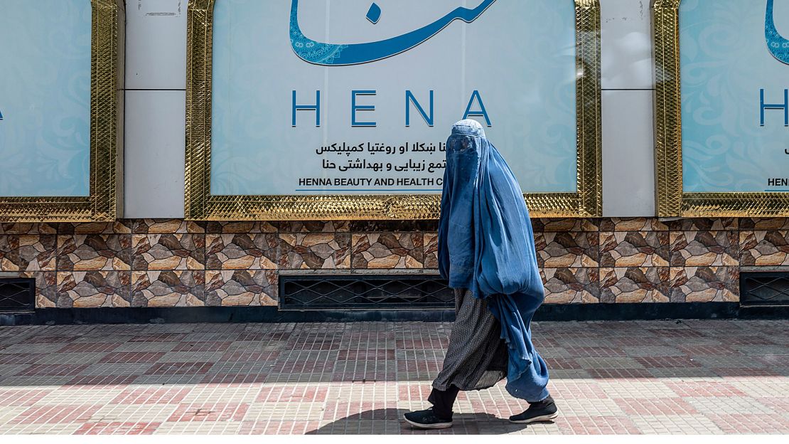 An Afghan burqa-clad woman walks past a beauty salon at the Shahr-e-Naw area in Kabul on July 25, 2023.