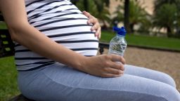 Pregnant woman outdoors holding bottle of water. She is sitting in the park