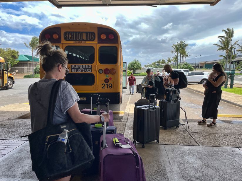 People arrive on school buses to evacuate the Maui airport on August 10.