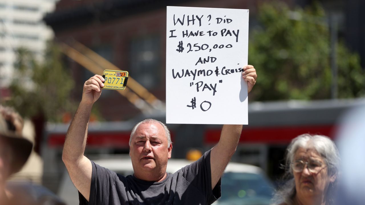 San Francisco taxi driver Matthew Sutter holds a sign and his taxi medallion during a protest outside of the California Public Utilities Commission (CPUC) on August 7, 2023 in San Francisco, California.  (Photo by Justin Sullivan/Getty Images)