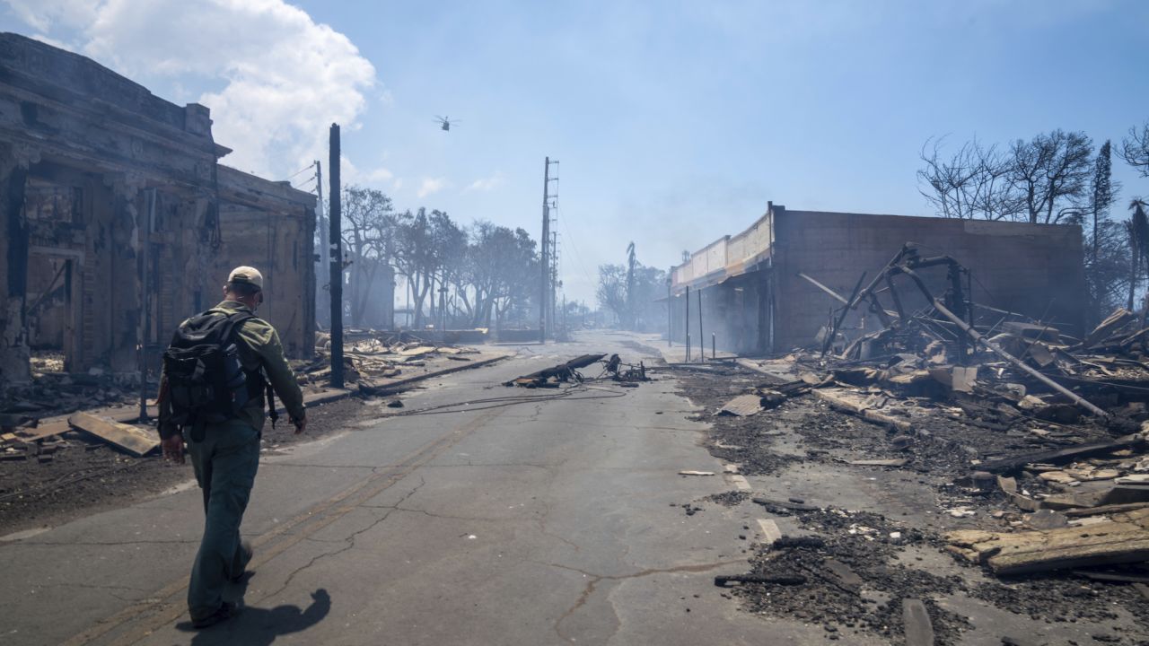 A man walks Wednesday past wildfire wreckage in Lahaina.