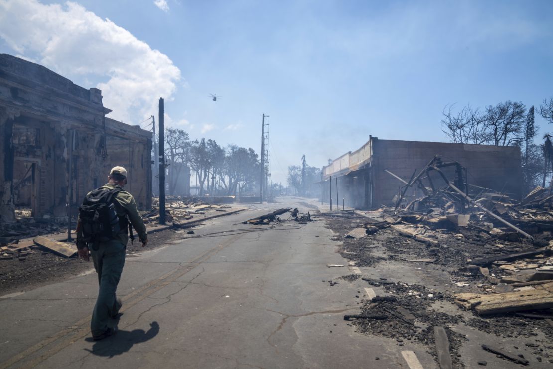 A man walks Wednesday past wildfire wreckage in Lahaina.