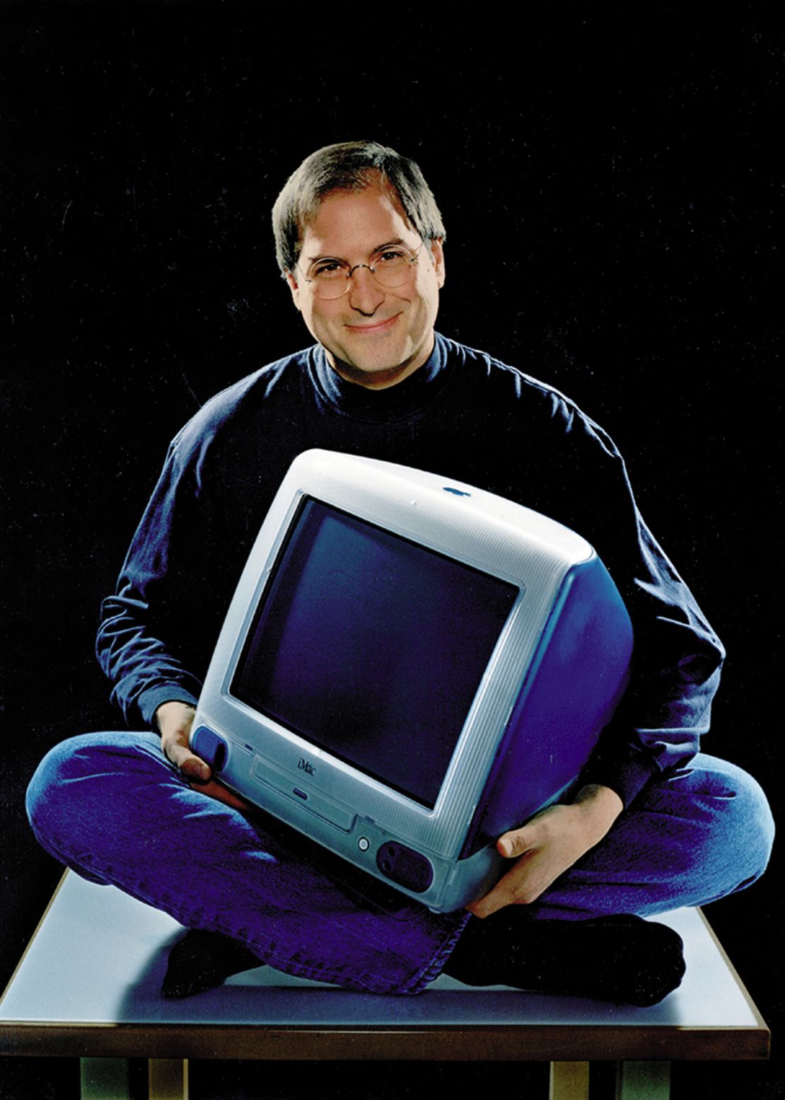 Feb. 19, 1999 - Cupertino, California, U.S. - Apple founder and current chief STEVE JOBS, cross legged and smiling as he holds the iMac that has become the hottest-selling computer on the market. The computer now comes in five fruit-inspired colors including blueberry and strawberry. Shown is the original Bondi Blue color.
