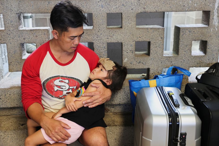 Vixay Phonxaylinkham holds his child Lana, 4, as she overheats while they await their flight to California at Kahului Airport, Hawaii on Thursday. Phonoxaylinkham, his wife, and their five children were caught in the Lahaina wildfires and survived by exiting their car and spending four hours in the ocean as the west Maui wildfires raged around them.