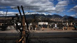 Downed power lines block a road as people feed chickens outside a burnt home in the aftermath of a wildfire in Lahaina, western Maui, Hawaii on August 11, 2023. A wildfire that left Lahaina in charred ruins has killed at least 67 people, authorities said on August 11, making it one of the deadliest disasters in the US state's history. Brushfires on Maui, fueled by high winds from Hurricane Dora passing to the south of Hawaii, broke out August 8 and rapidly engulfed Lahaina. 