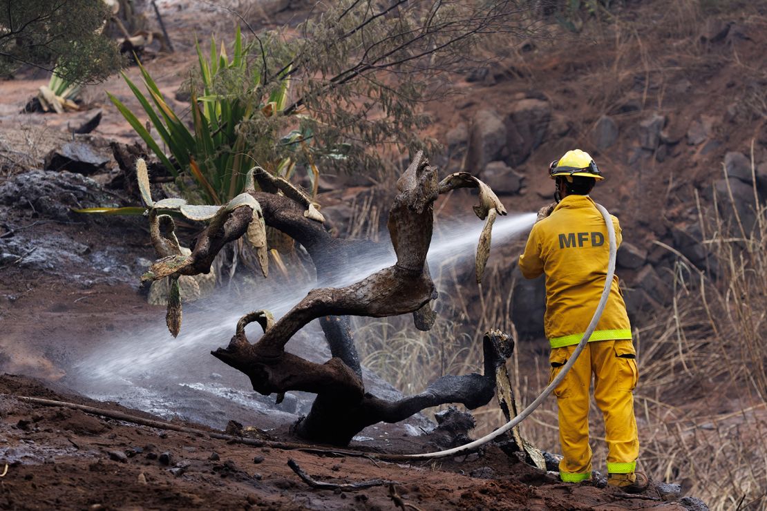 A Maui County firefighter battles flare-up fires in a canyon in Kula on Maui on Sunday.