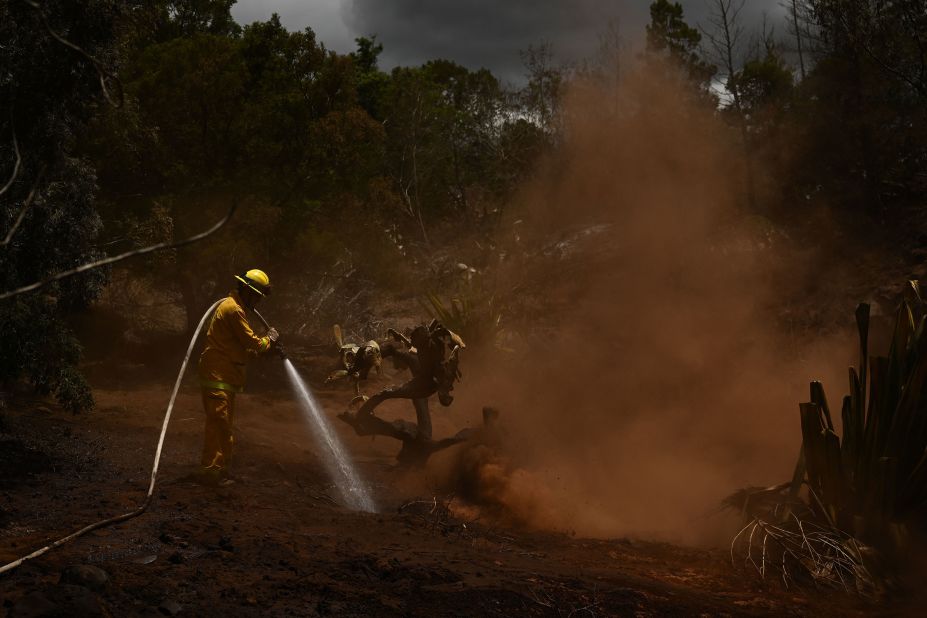 A Maui County firefighter extinguishes a fire near homes in Kula, Hawaii, on August 13.