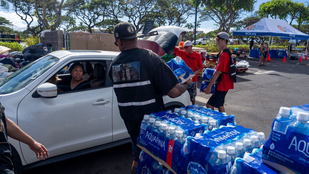 A woman collects water at a shopping center in Lahaina where different groups are handing out supplies.