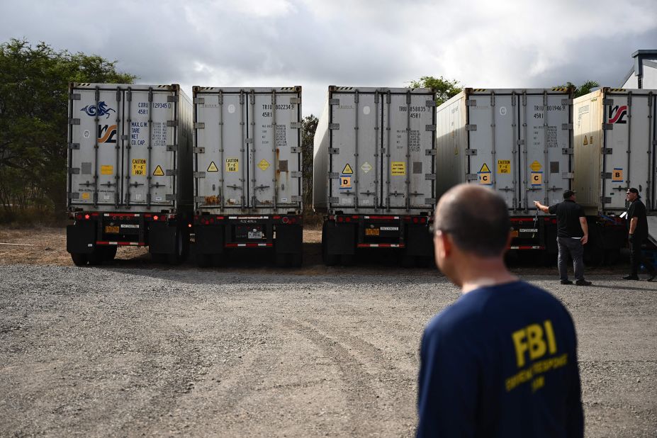 An FBI agent watches as two additional refrigerated storage containers arrive next to the Maui Police Forensic Facility where human remains were being stored in Wailuku, Hawaii, on Monday, August 14.