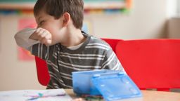Boy blowing nose in classroom - stock photo
