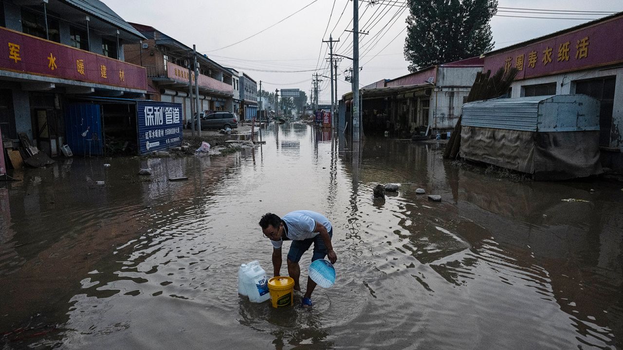 Un barbat trece prin apele de inundatii in retragere pe o strada din Zhuozhou pe 5 august.