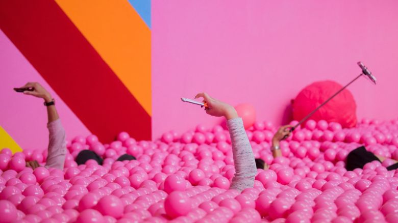 Visitors use their mobile devices to take pictures of themselves posing in a pink ball bath at the Supercandy Pop-Up Museum in Cologne, western Germany, on September 27, 2018. - Until December 30, 2018, the museum offers 20 interactive installations for visitors to do selfies and to post them on Instagram or other social media platforms. - Germany OUT (Photo by Rolf Vennenbernd / dpa / AFP) / Germany OUT (Photo by ROLF VENNENBERND/dpa/AFP via Getty Images)