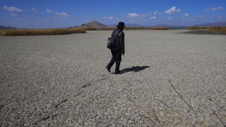 An Aymara man walks on the dry cracked bed of Lake Titicaca, in Huarina, Bolivia, Thursday, July 27, 2023.  The lake's low water level is having a direct impact on the local flora and fauna and is affecting local communities that rely on the natural border between Peru and Bolivia for their livelihood.  (AP Photo/Juan Karita)