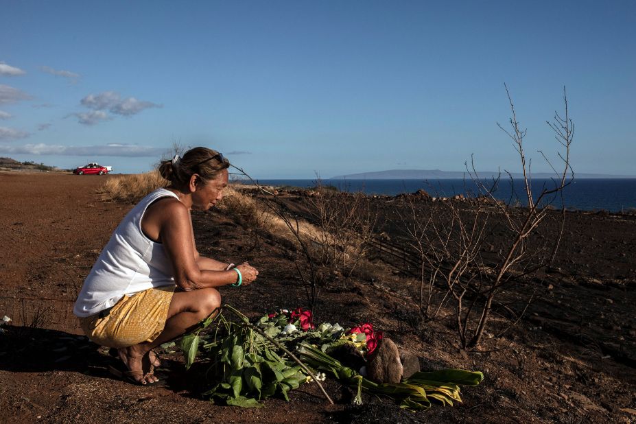 A woman lays down flowers and prays on a hillside overlooking the rubble of Lahaina on August 16.