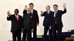  Тогавашният бразилски президент Жаир Болсонаро, руският президент Владимир Путин, китайският лидер Си Дзинпин, индийският премиер Нарендра Моди и президентът на Южна Африка Сирил Рамафоса махат за натиск по време на срещата на върха на БРИКС в Бразилия през 2019 г. 