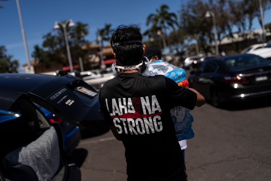 Ken Alba carries a bag of ice at a food and supply distribution center that was set up in the parking lot of a Lahaina shopping mall on Thursday, August 17.