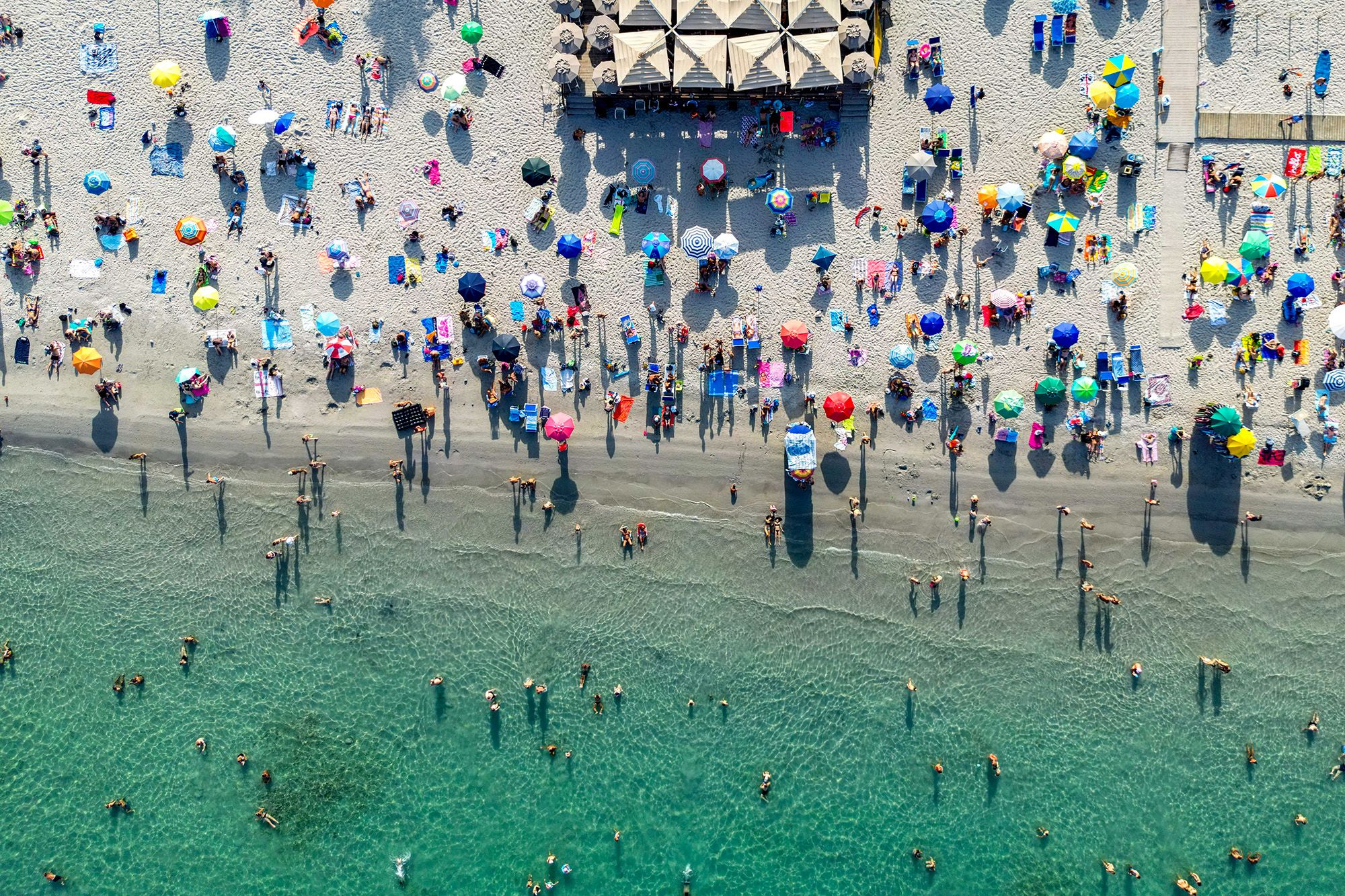 Visitors swim in the sea and sit in the shade of parasols on Poetto beach in Cagliari, Sardinia, Italy, on Wednesday, July 19, 2023. Temperatures in Cagliari touched 45.9C(115F), closing in on Europe's record of 48.8C. Photographer: Francesca Volpi/Bloomberg via Getty Images