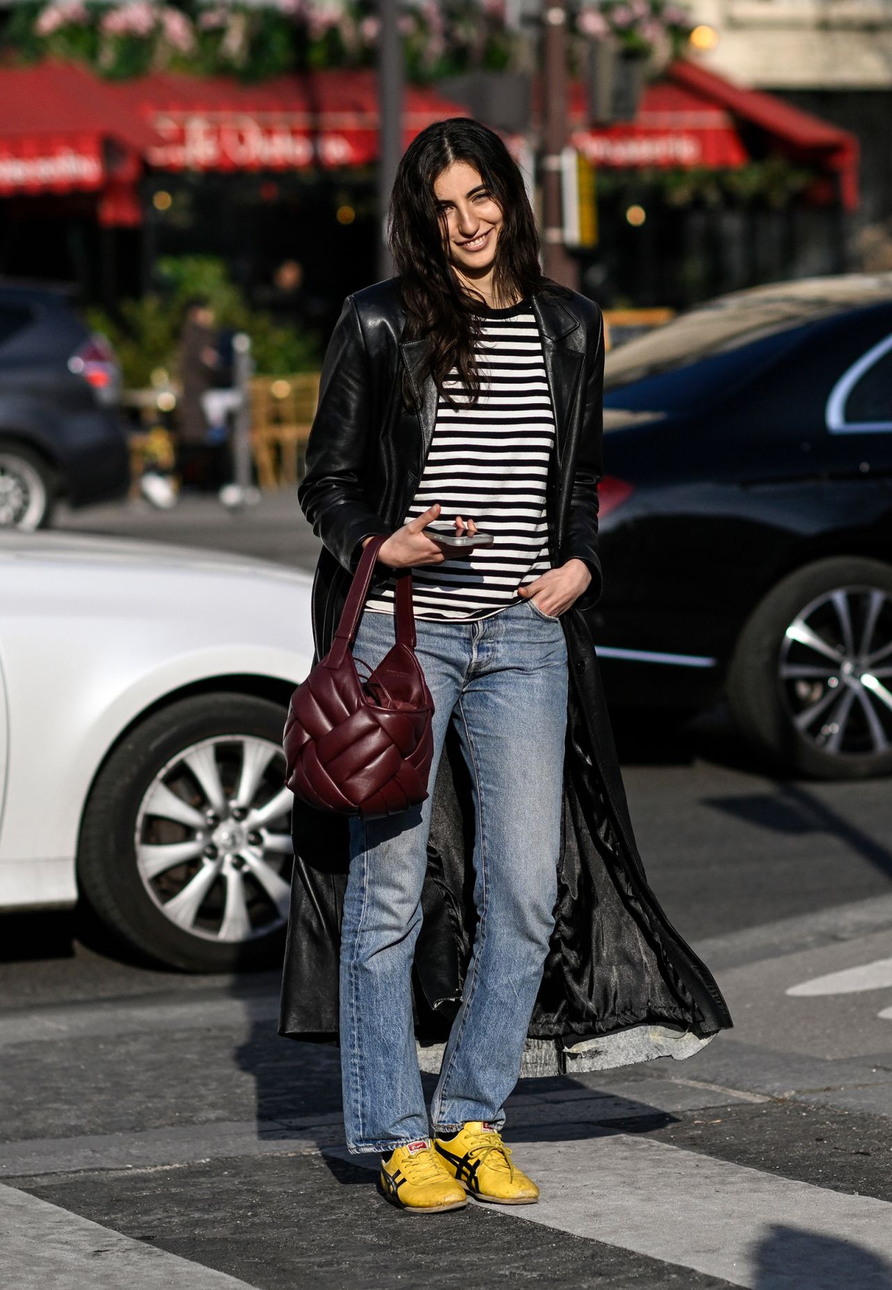 PARIS, FRANCE - MARCH 01: A model is seen wearing a black leather coat, black and white striped shirt, blue jeans and yellow sneakers with a maroon bag outside the Dries Van Noten show during Paris Fashion Week F/W 2023 on March 01, 2023 in Paris, France. (Photo by Daniel Zuchnik/Getty Images)