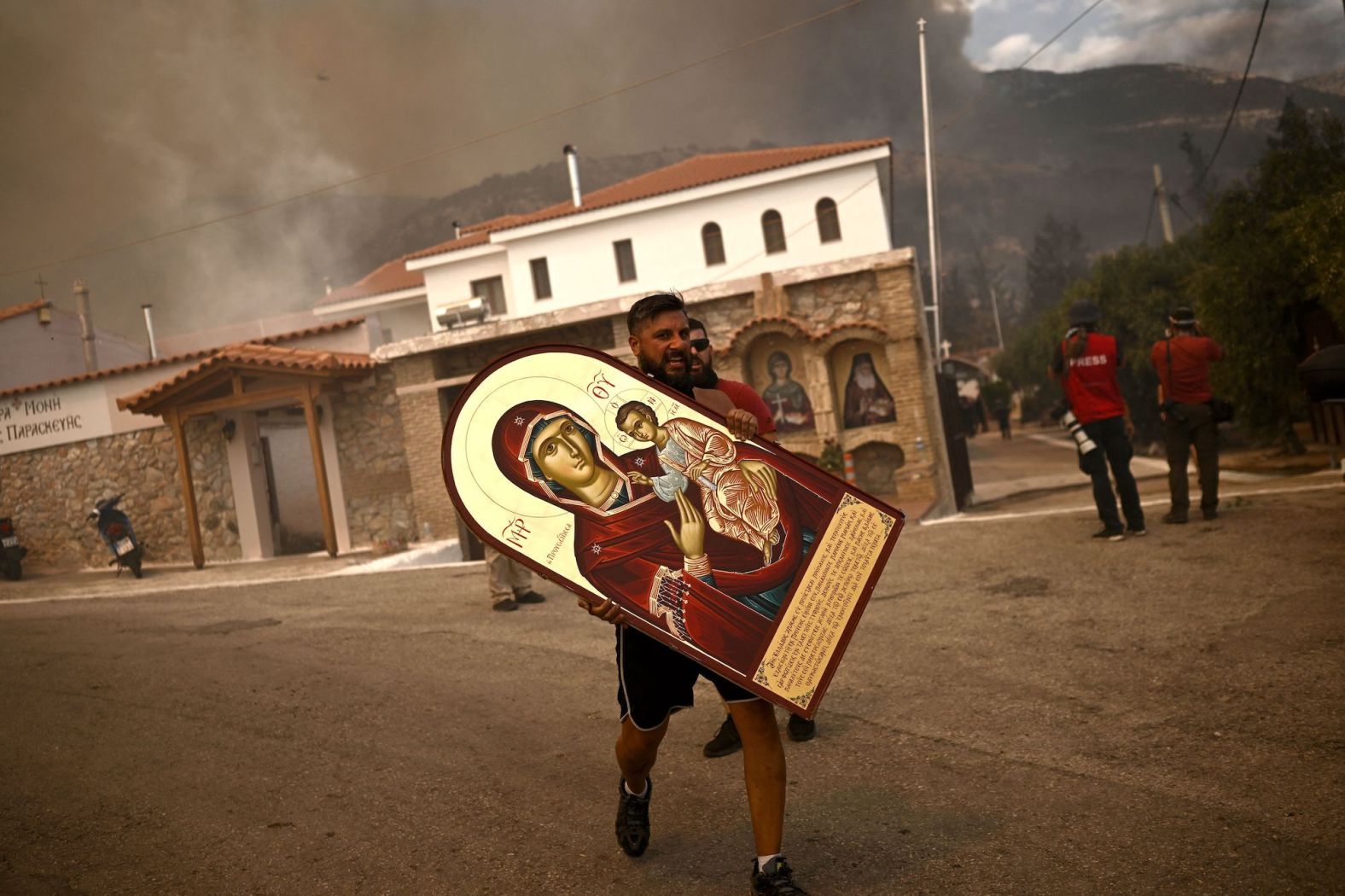 A volunteer carries an icon from a burning monastery as a wildfire spreads in Acharnes on Wednesday, August 23.