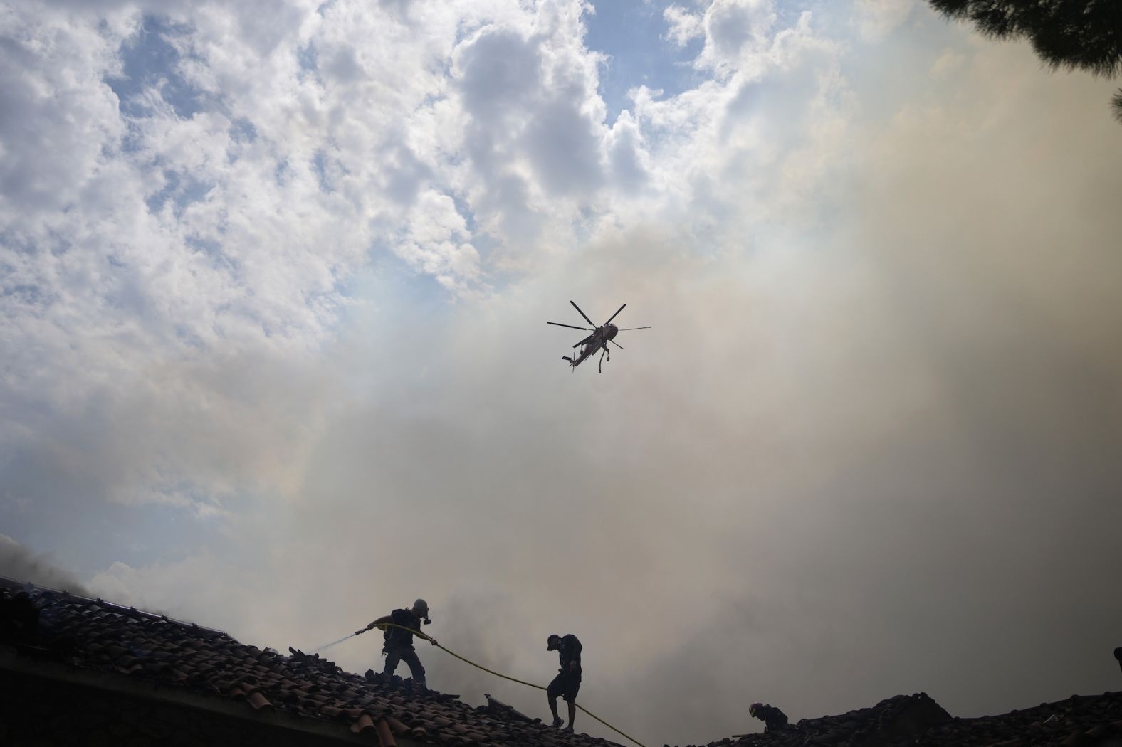 A firefighting helicopter flies over firefighters in Acharnes on August 23.