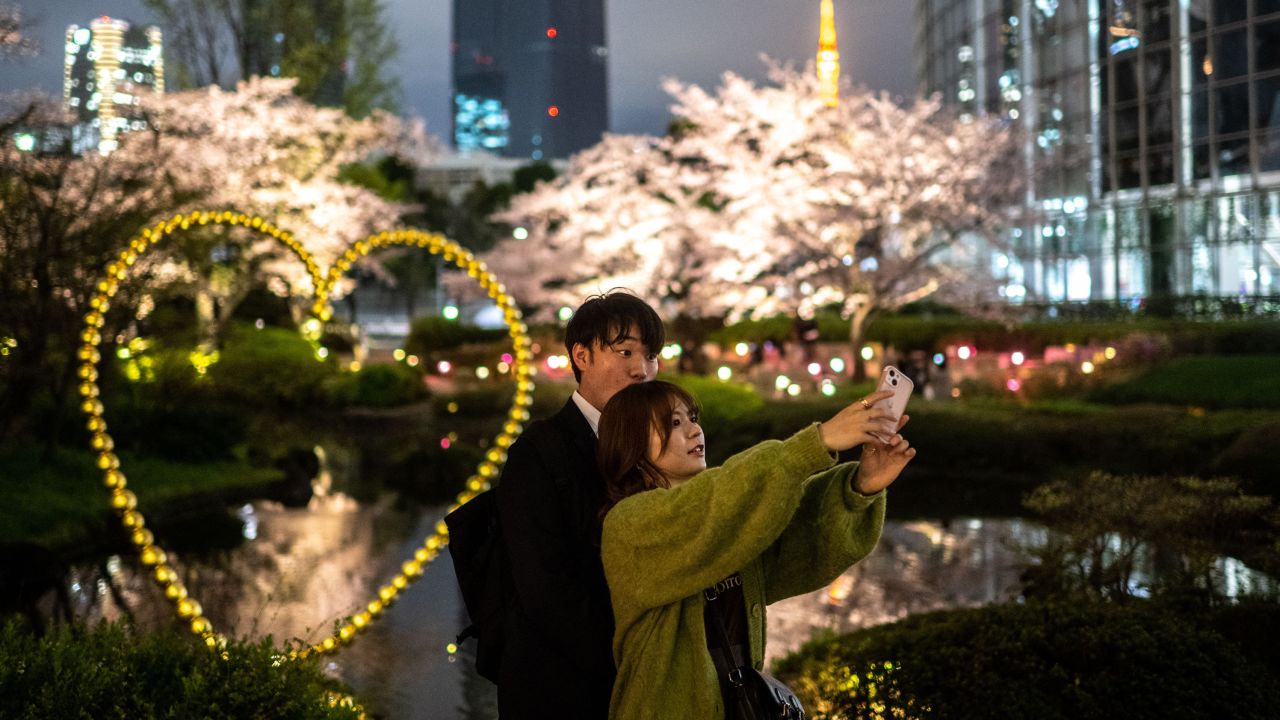 A couple photographs cherry blossoms in Roppongi district of Tokyo on March 29, 2023. 