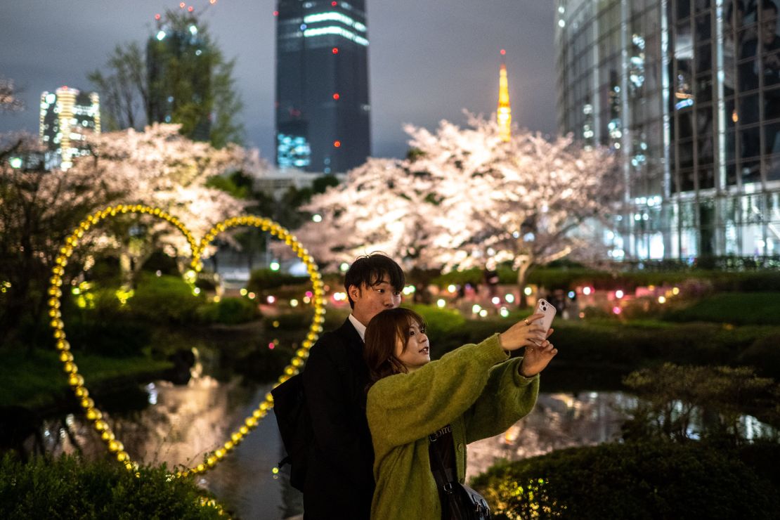 A couple photographs cherry blossoms in Roppongi district of Tokyo on March 29, 2023. 