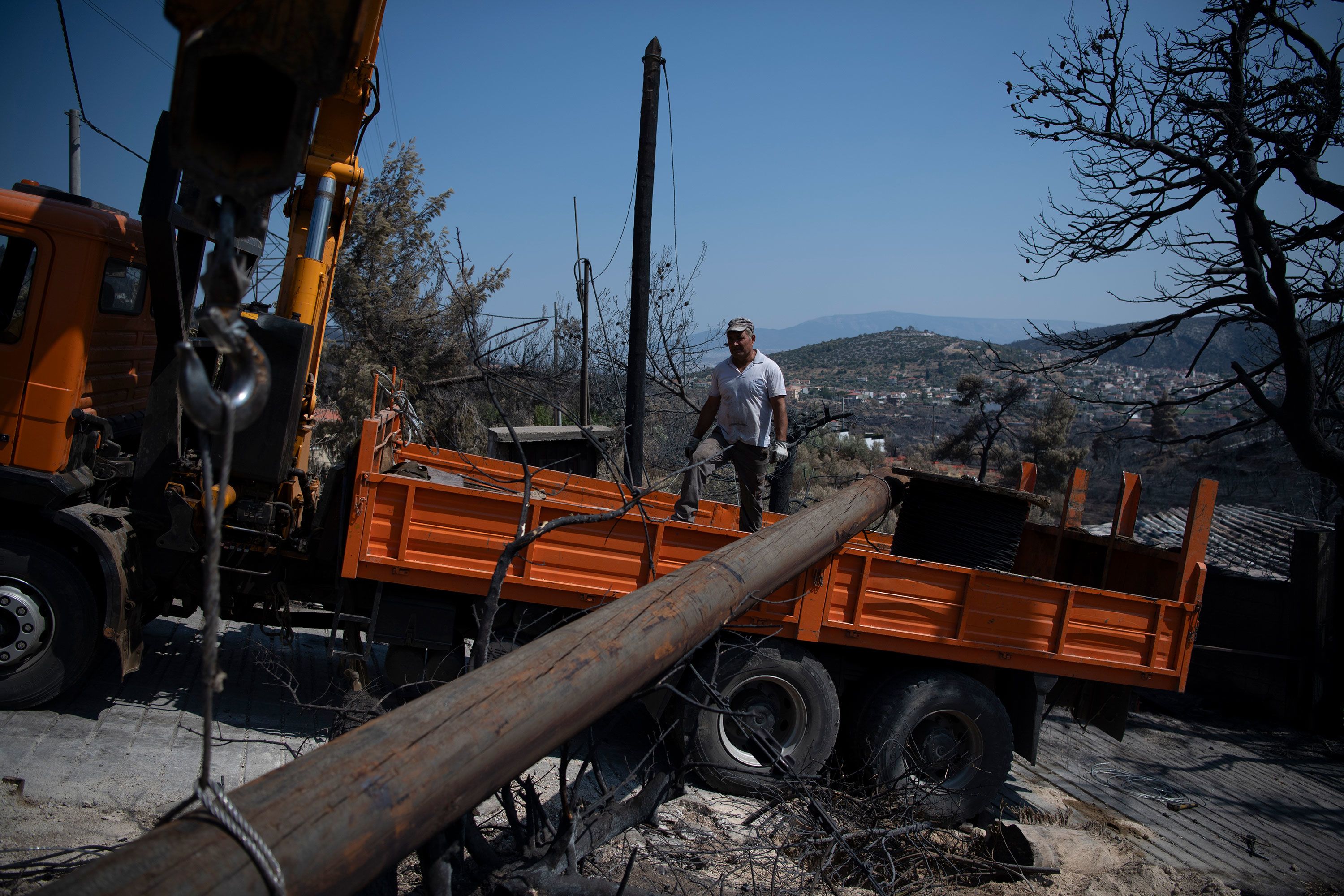 Electric company workers replace a utility pole after a wildfire in Fyli on August 25.