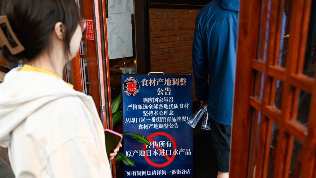 People walk into an area of Japanese restaurants past a sign reading "Suspend the sale of all fish products imported from Japan", in Beijing on August 27, 2023.