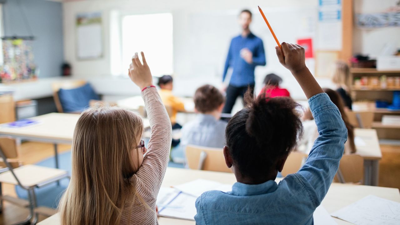 Rear view of students sitting with hands raised in classroom