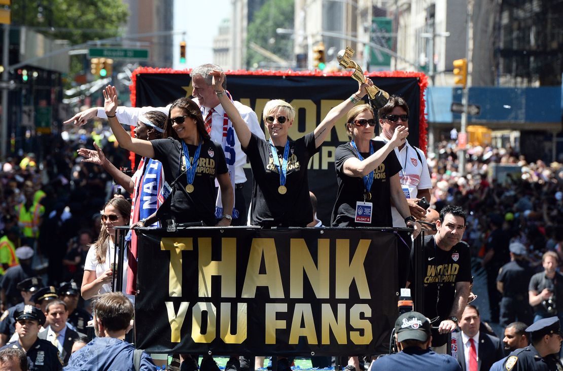 USA women's soccer team midfielder Megan Rapinoe (C) holds up the World Cup 2015 trophy as midfielder Carli Lloyd (2nd L), New York City Mayor Bill de Blasio and head coach Jill Ellis (R) wave to the crowd during the ticker tape parade in New York on July 10, 2015. AFP PHOTO/JEWEL SAMAD        (Photo credit should read JEWEL SAMAD/AFP via Getty Images)