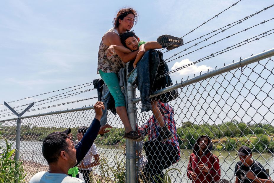 Migrants climb over a barbed wire fence after crossing the Rio Grande from Mexico into Eagle Pass, Texas, on Friday, August 25.