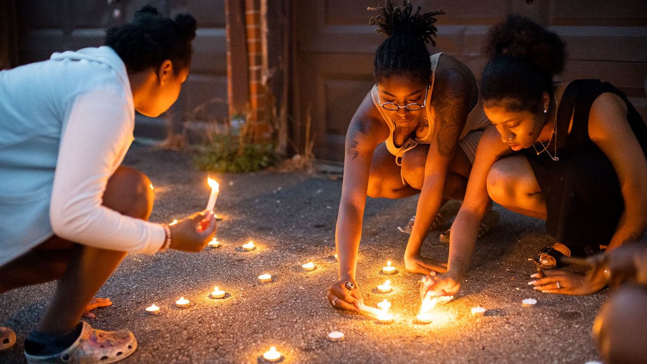 Sandriana McBroom, derecha, y Makhiya Mcbroom, centro, encienden velas que deletrean