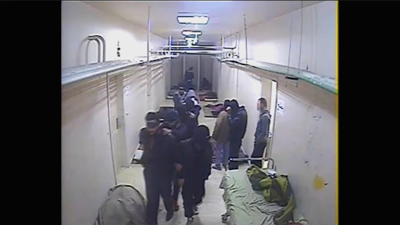 Otra imagen de la cámara de seguridad muestra a hombres en un pasillo.  CNN ha difuminado un rostro en esta imagen, proporcionada por CIJA, para ocultar la identidad de la persona.