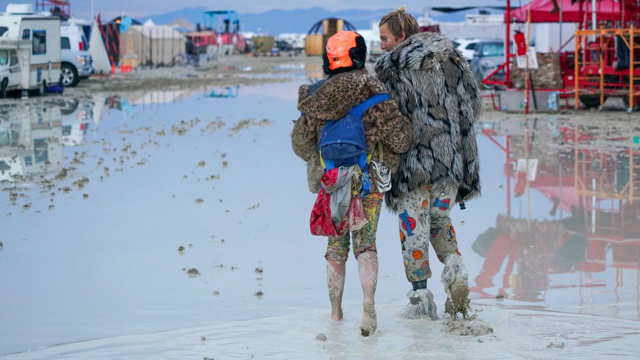 Participanții la Burning Man merg sâmbătă prin noroi.