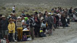 People wait for a shuttle bus to take them to Gerlach and Reno on the side of Highway 34 out near the Burning Man site on the Black Rock Desert in northern Nevada on September 3, 2023.